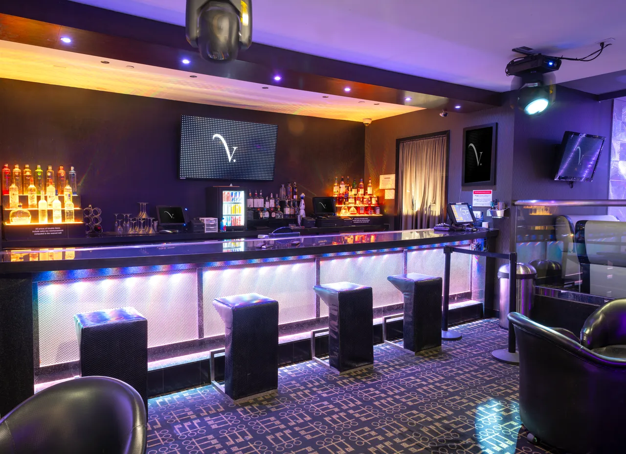 Venue 412 main bar with a backlit silver bar front, gold accent ceiling lighting, and the venue's bottle inventory on display behind the bartender station.