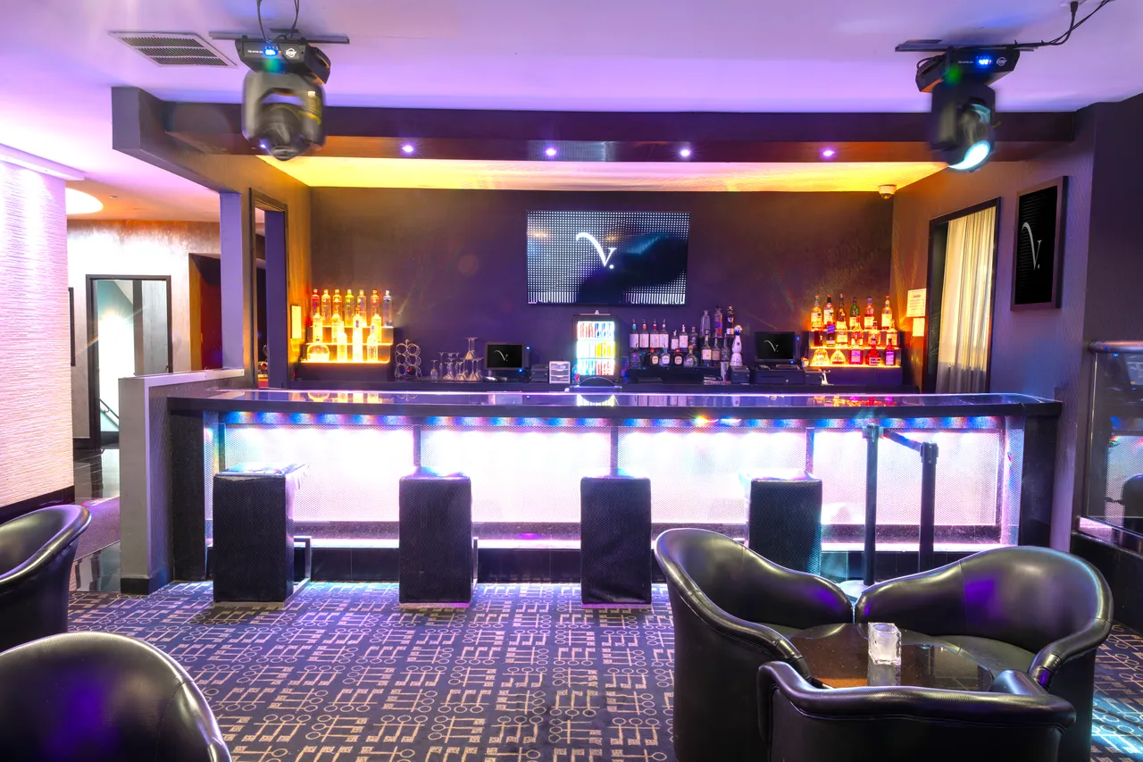 Venue 412 bar with the silver illuminated front, leather bar stools, full liquor display, and a TV mounted above showing the venue logo.