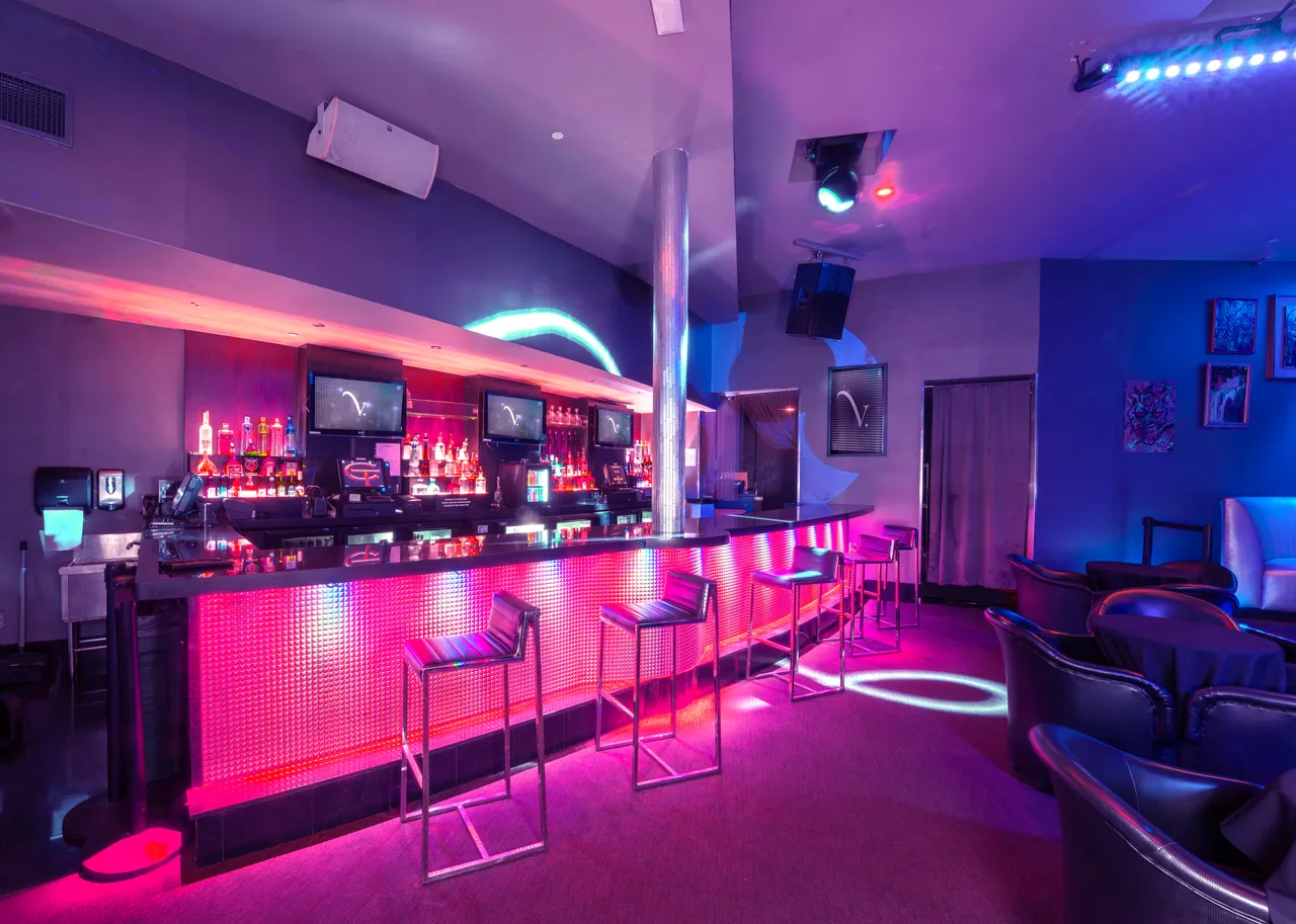 Venue 412 bar lit in pink and magenta LED, bar stools across the front, and lounge chairs in the foreground for bottle service seating.