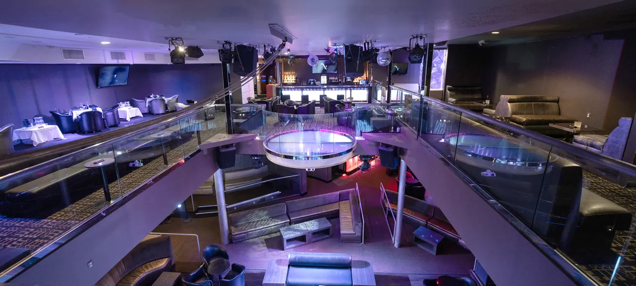 Venue 412 in San Francisco — elevated panoramic view of the two-level main room with mezzanine dining tables on the left, the round glass dance floor centerpiece, the bar at the back, and bottle service lounge banquettes throughout.