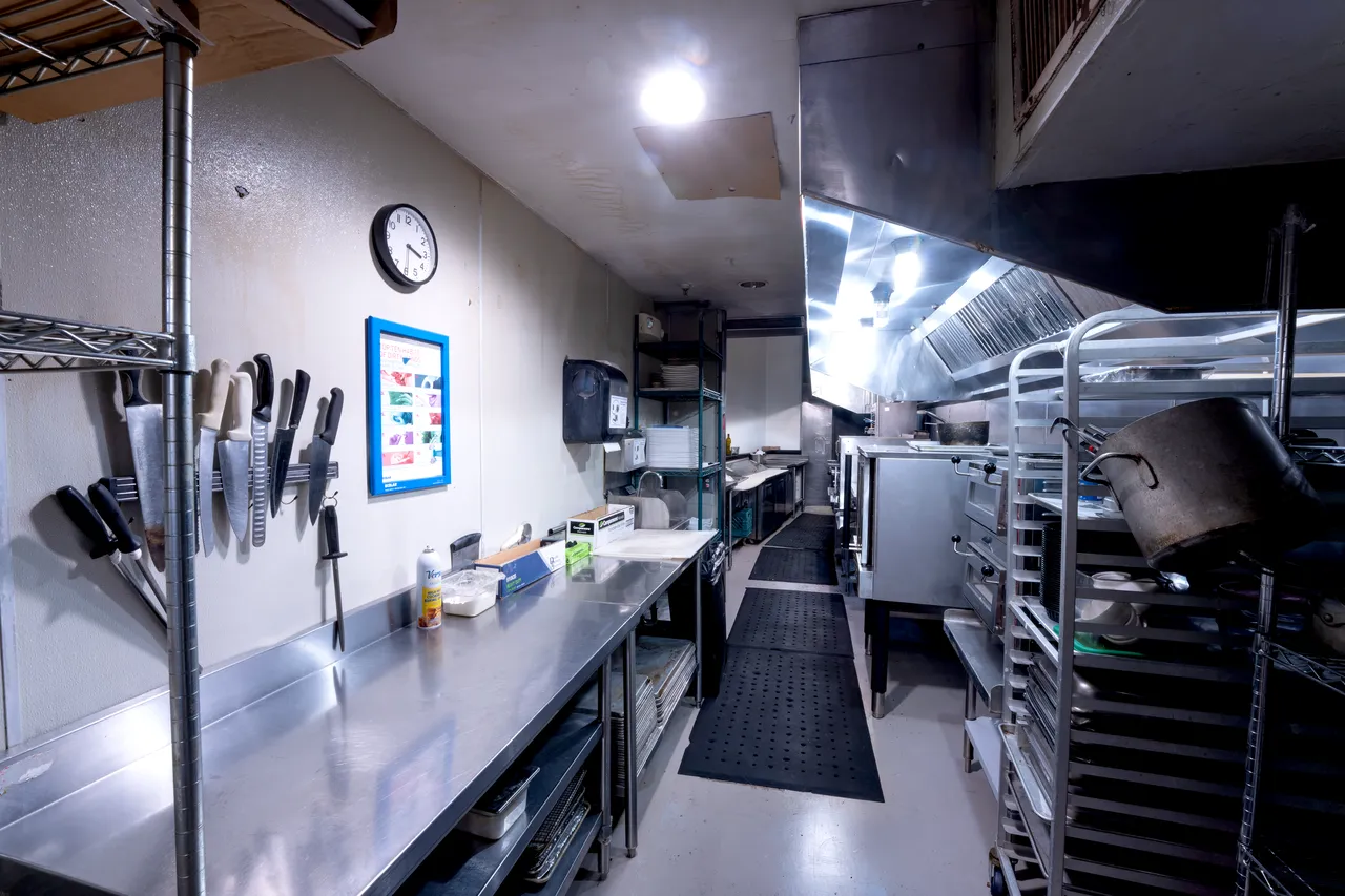 Venue 412 commercial kitchen cold-prep line — knife wall, stainless prep tables, and dish-out racks for plated service.