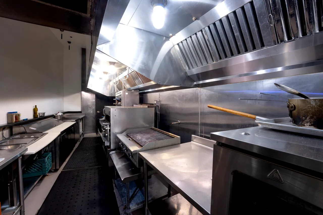 Venue 412 commercial kitchen cooking line — stainless hood vent, flat-top grill, oven bank, and prep surfaces for in-house catering.