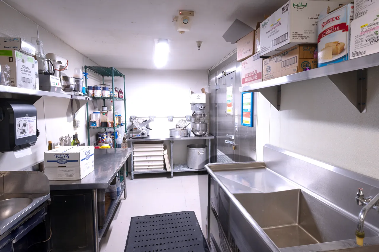 Venue 412 commercial kitchen prep and storage area in San Francisco — wire shelving with ingredient inventory, stand mixer, and stainless prep stations.